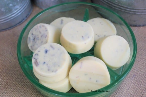 A green glass dish holding several round, white solid lotion bars with small specks visible throughout each bar.