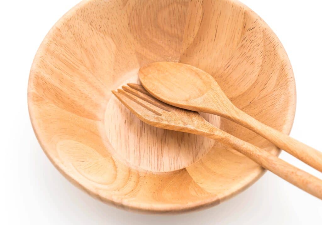 A wooden bowl with a wooden fork and spoon resting inside, set against a white background.