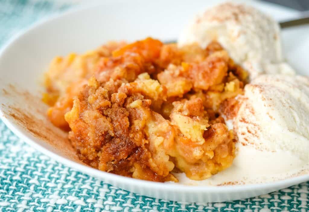 A plate with peach cobbler topped with cinnamon and served alongside two scoops of vanilla ice cream.