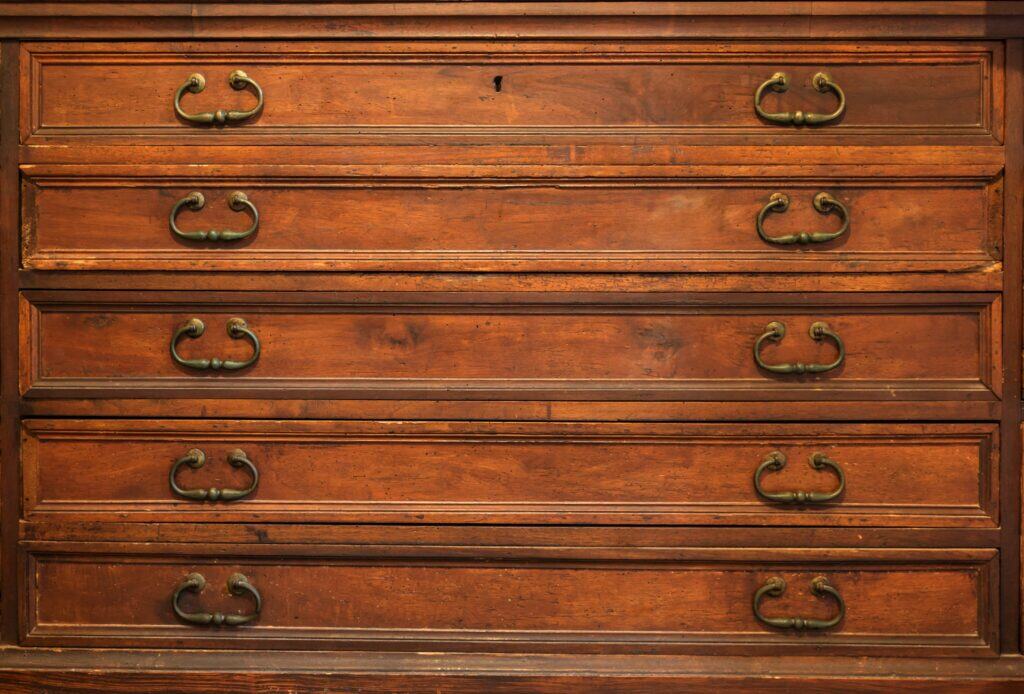 A close-up view of a vintage wooden dresser with five drawers, each featuring two metal handles.