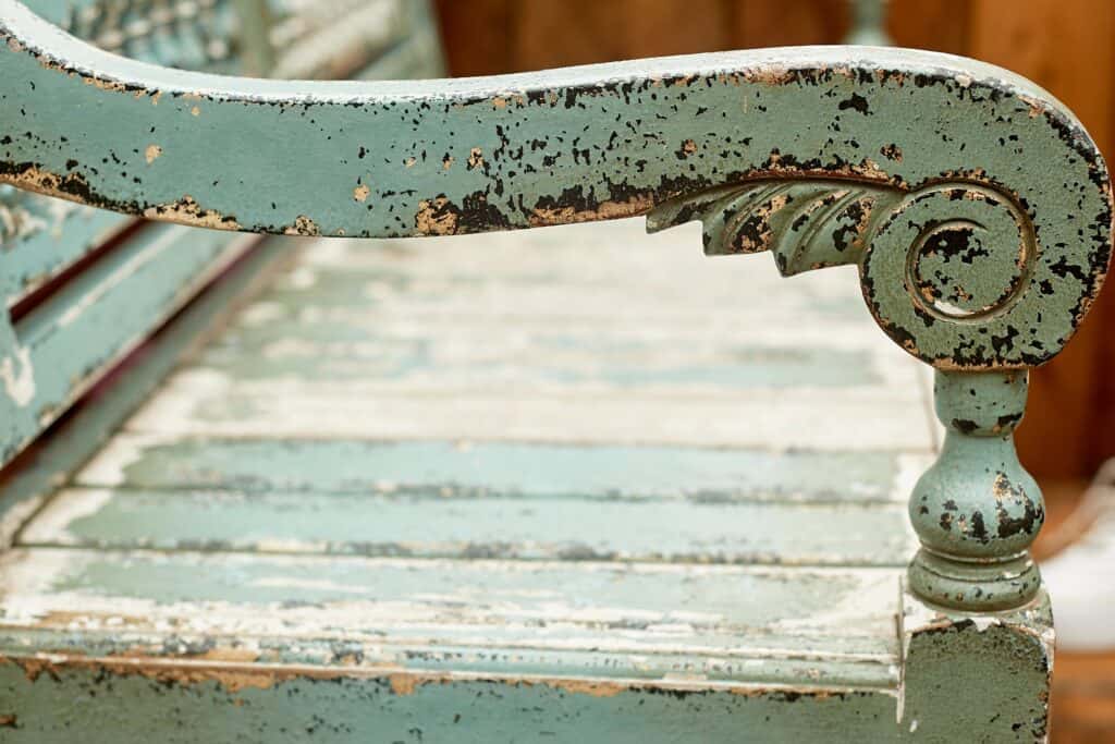 Close-up of the armrest and seat of an old, weathered wooden bench with peeling light blue paint and visible wood grain.