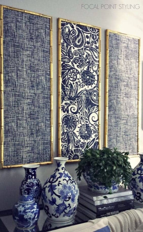 Three framed blue and white textile panels hang on a wall above a surface displaying blue and white ceramic vases and a potted green plant.