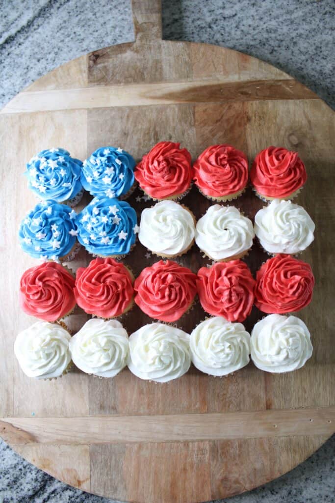 Twenty cupcakes arranged in a rectangle with blue, red, and white icing to resemble the American flag on a wooden board.