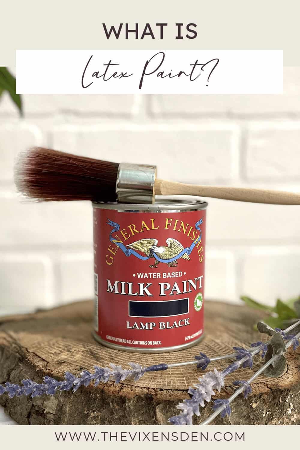 A can of General Finishes water-based milk paint in lamp black with a paintbrush resting on top, placed on a wooden surface with decorative leaves.