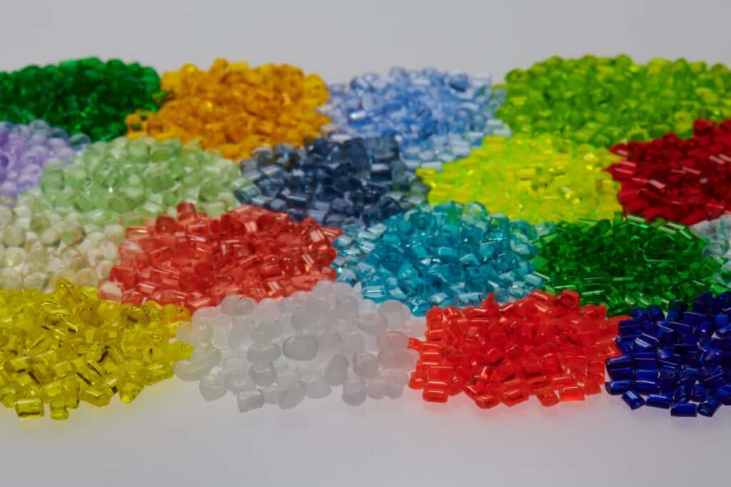 Assorted small plastic resin pellets in various colors arranged in clusters on a white surface.