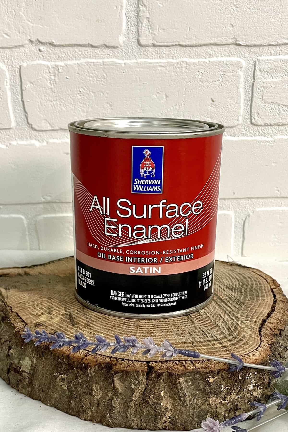 A can of Sherwin-Williams All Surface Enamel sits on a wooden slab with a white brick background and some lavender in the foreground.