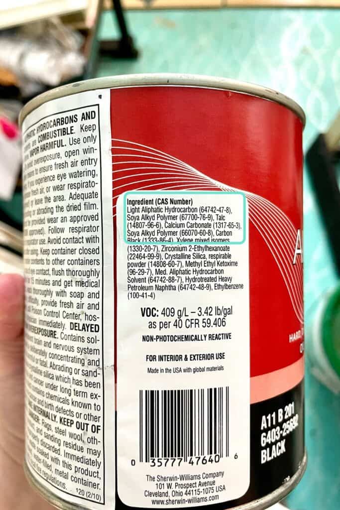 A close-up of a can showing an ingredients list, product information, warnings, and a barcode. The can is being held in someone’s hand.