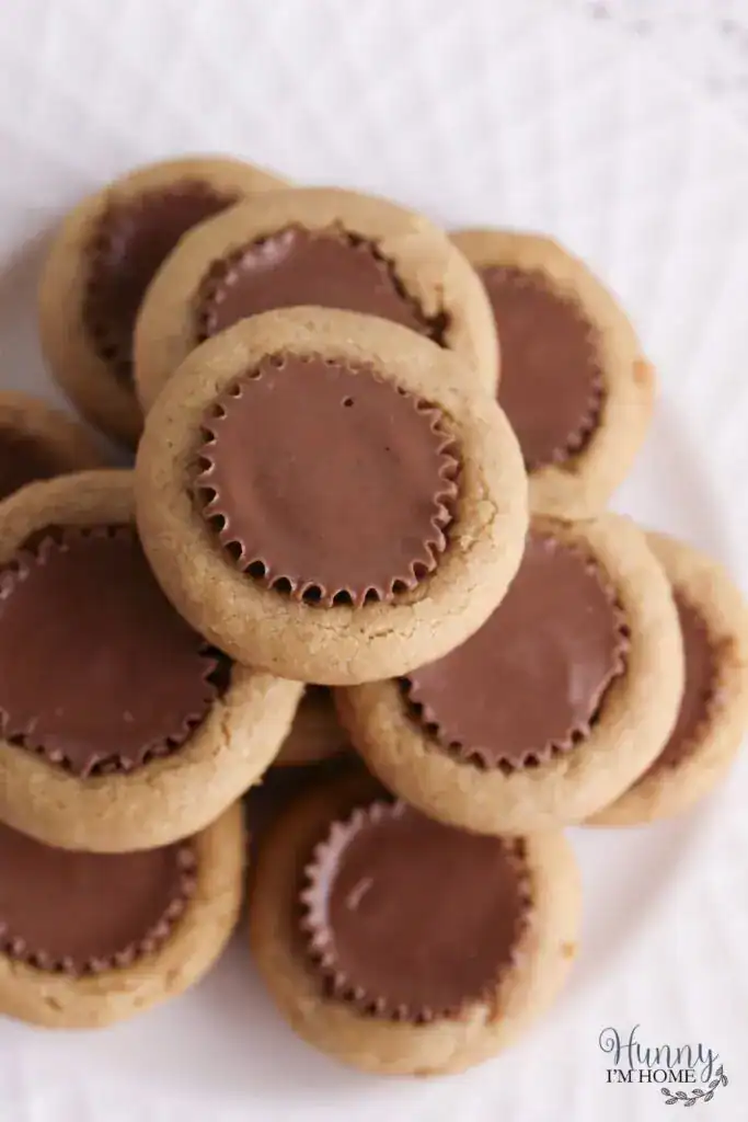 A stack of peanut butter cookies with chocolate peanut butter cups pressed into the center, arranged on a white plate.