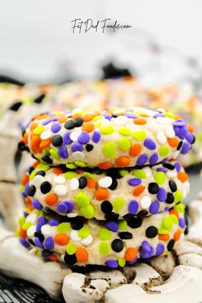 A stack of cookies covered in orange, purple, green, white, and black sprinkles sits on a decorative white skeleton hand.