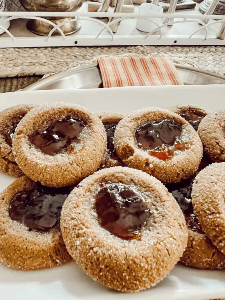 A plate of round cookies with a jam-filled center arranged on a white tray, with kitchen items visible in the background.