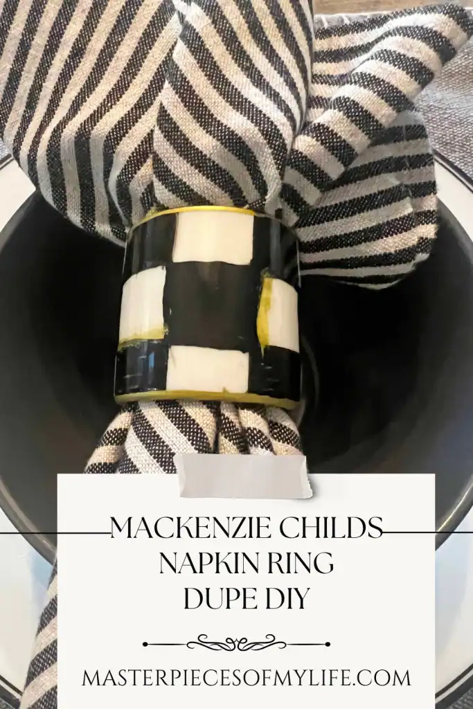 Black and white checkered napkin ring holding a striped napkin, displayed over a black plate, with text reading "Mackenzie Childs Napkin Ring Dupe DIY.