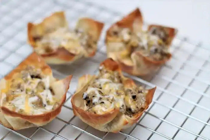 Four wonton cups filled with a ground meat and cheese mixture rest on a metal cooling rack.
