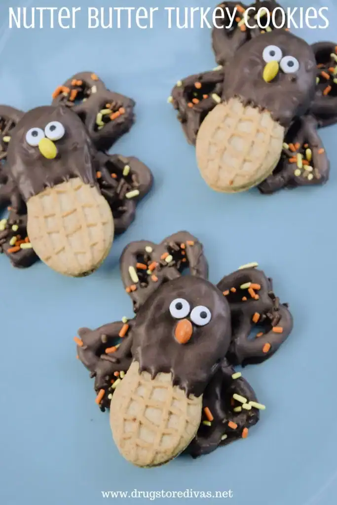 Three Nutter Butter turkey cookies with chocolate-dipped pretzels as feathers, candy eyes, yellow beaks, and orange candy noses on a blue plate.